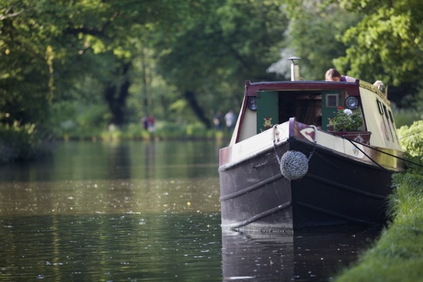 A brown and red narrowboat on a quiet river with trees overhead