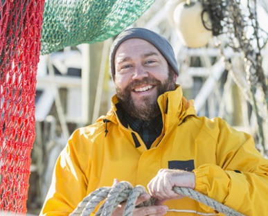 Fisherman Coiling A Large Rope Around His Hand With Red And Green Netting Drapped Behind
